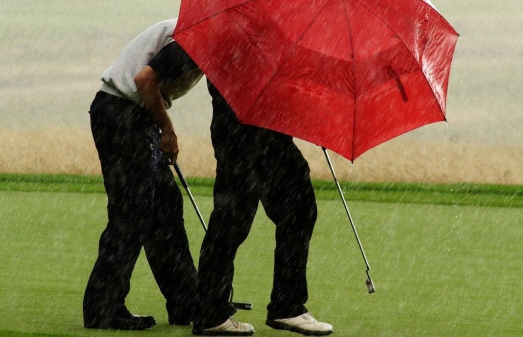 Two golfers hiding from the rain behind their red best golf umbrella