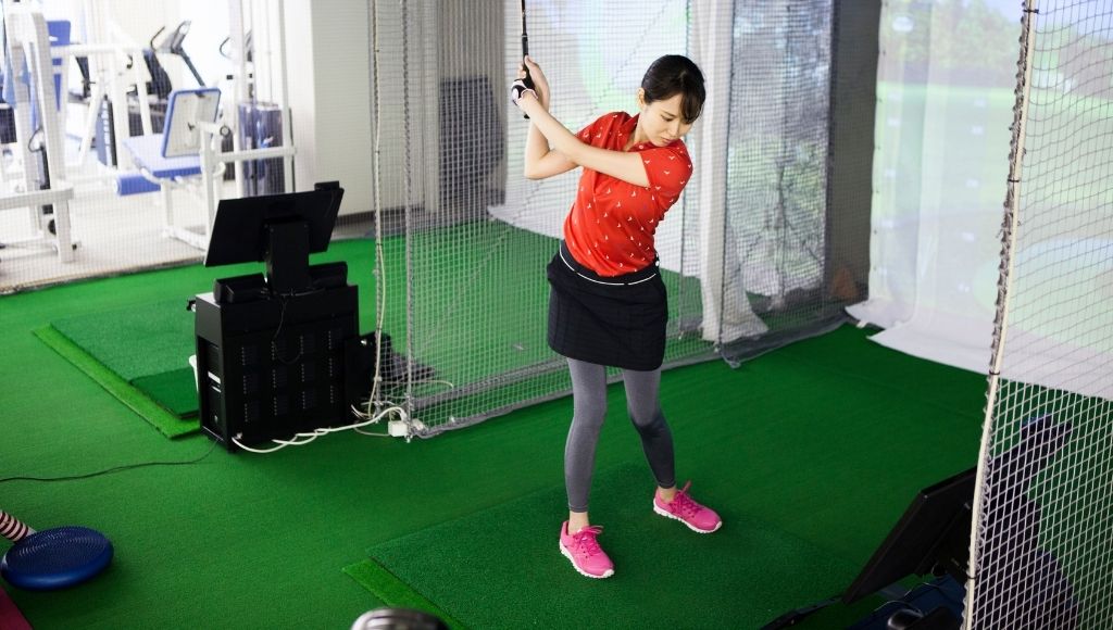 A lady playing golf in an indoor golf simulator