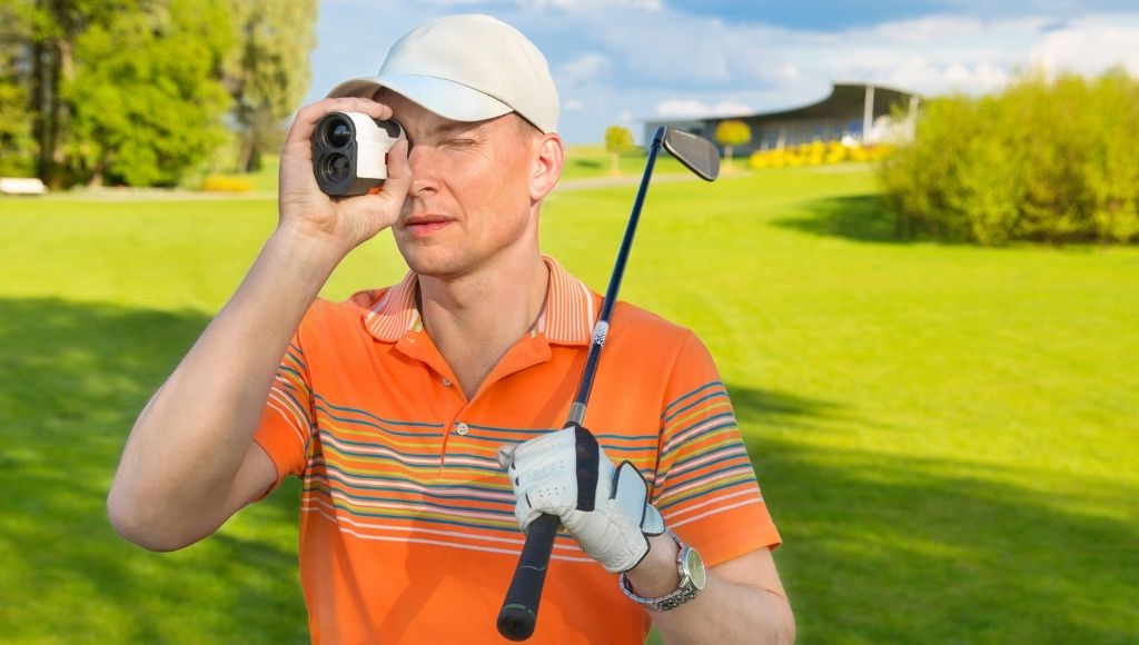 A man stands with a golf stick on his shoulder and looking for a ball with bushnell pro xe golf rangefinder