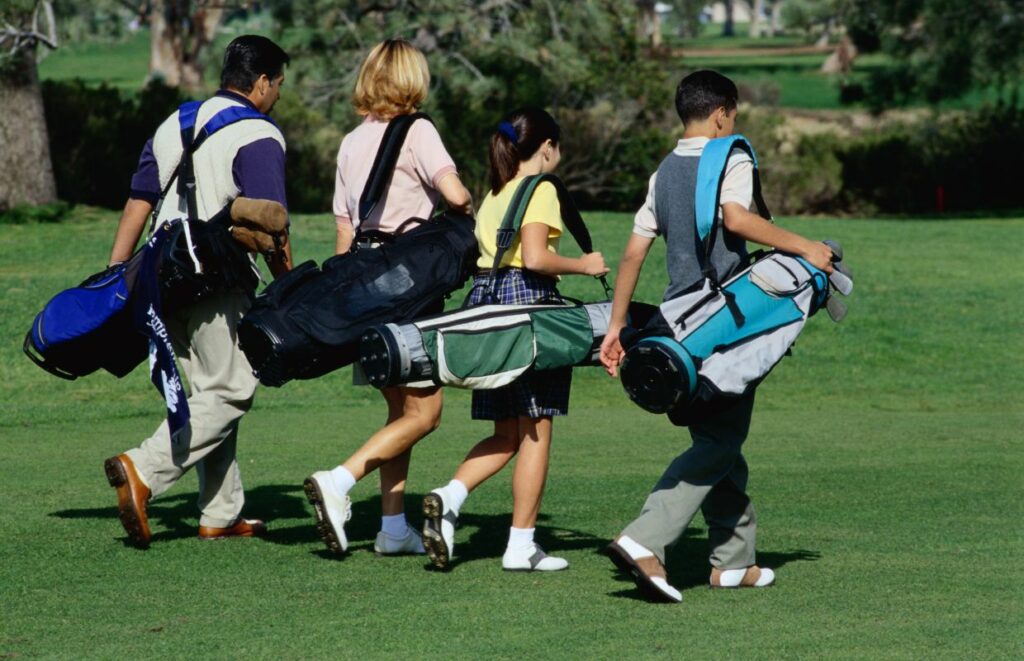 4 people walking on a golf course carrying a single strap golf bag