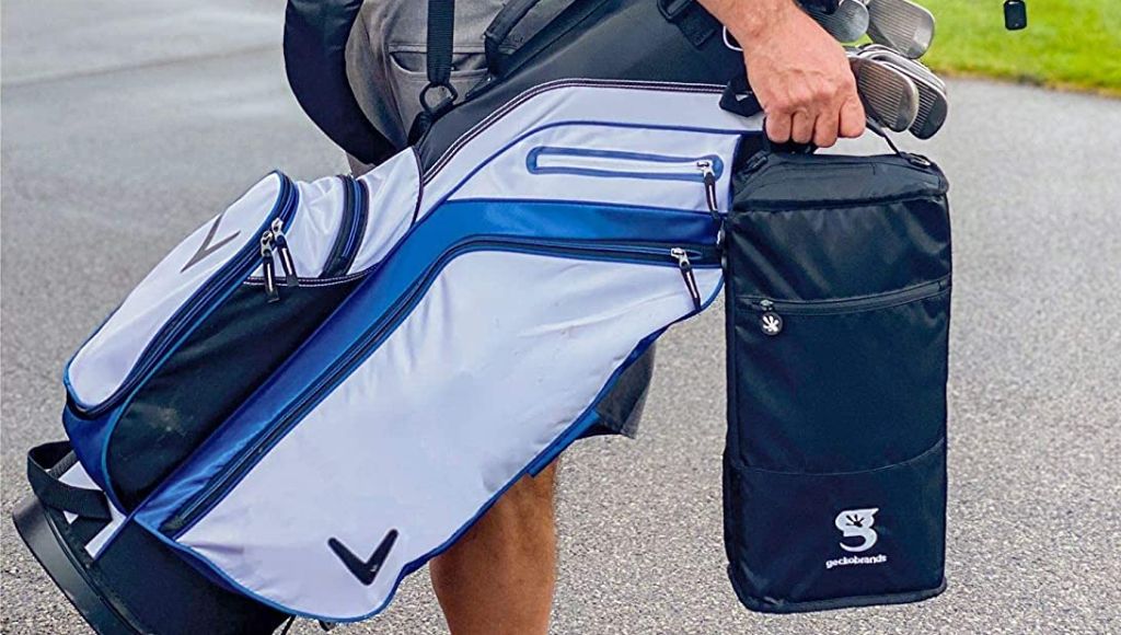 A golfer stands with a golf bag over his shoulder and an ice cooler bag in his hand