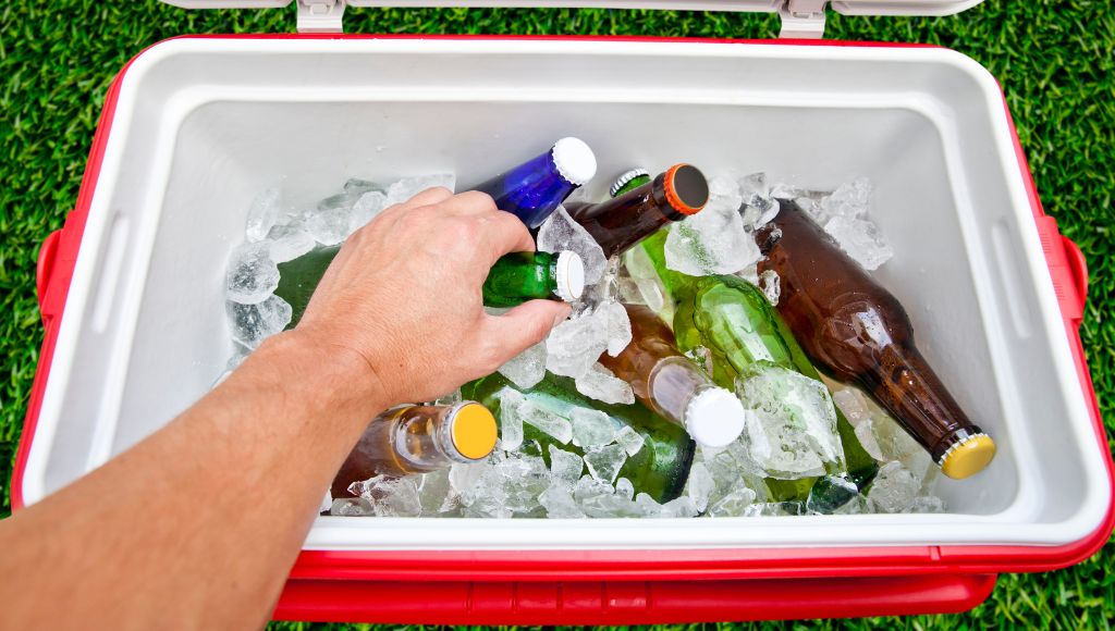 A hand picks up a beer from a drink cooler box filled with beer
