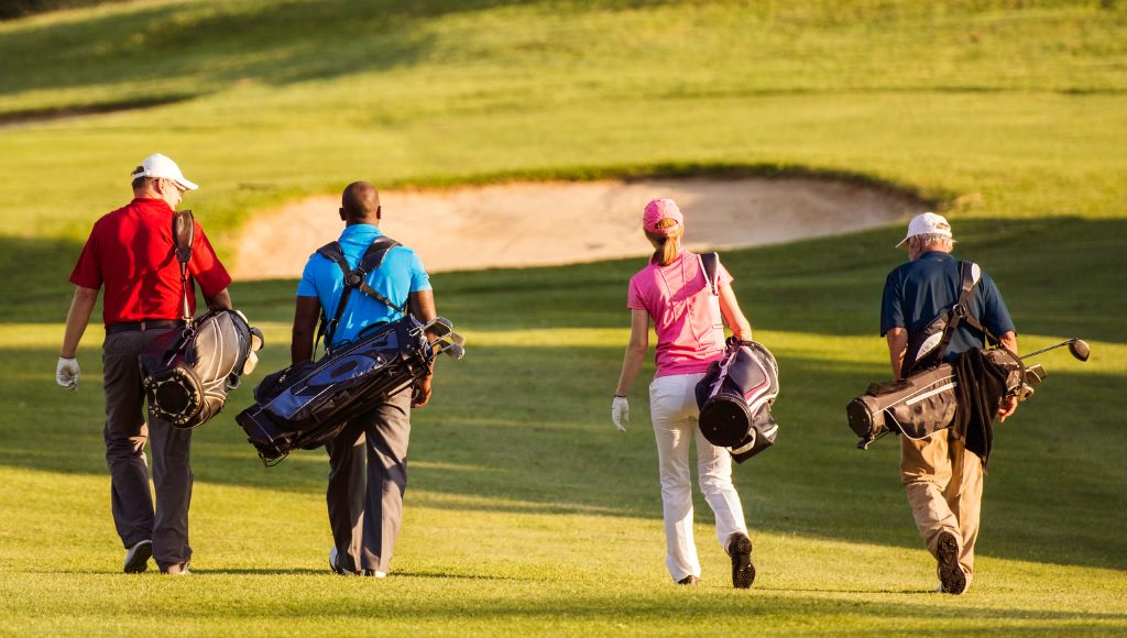 Four friends on golf course carrying their golf bag