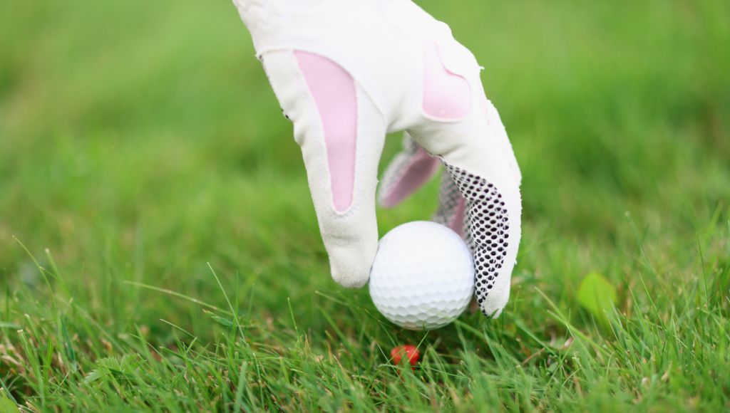 Hand in golf glove puts the ball on a golf tee