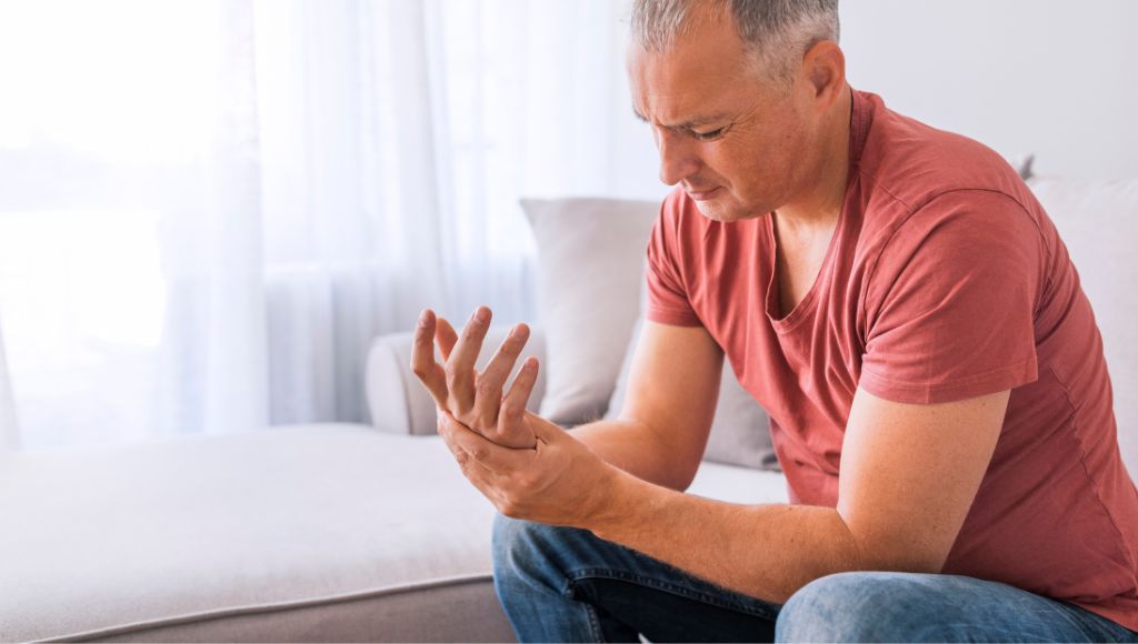 A man suffering from wrist pain at home while sitting on sofa during the day