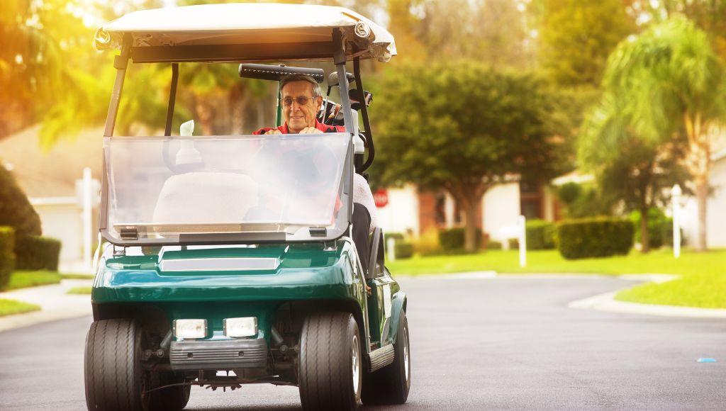 Senior man driving golf cart in suburbs on a golf community road