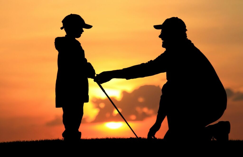 A dad and his son golfing at sunset