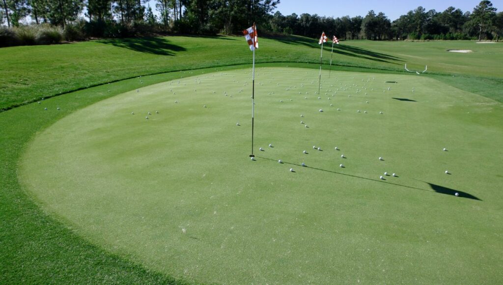 A golf green with lots of balls from practise shots close to the flag